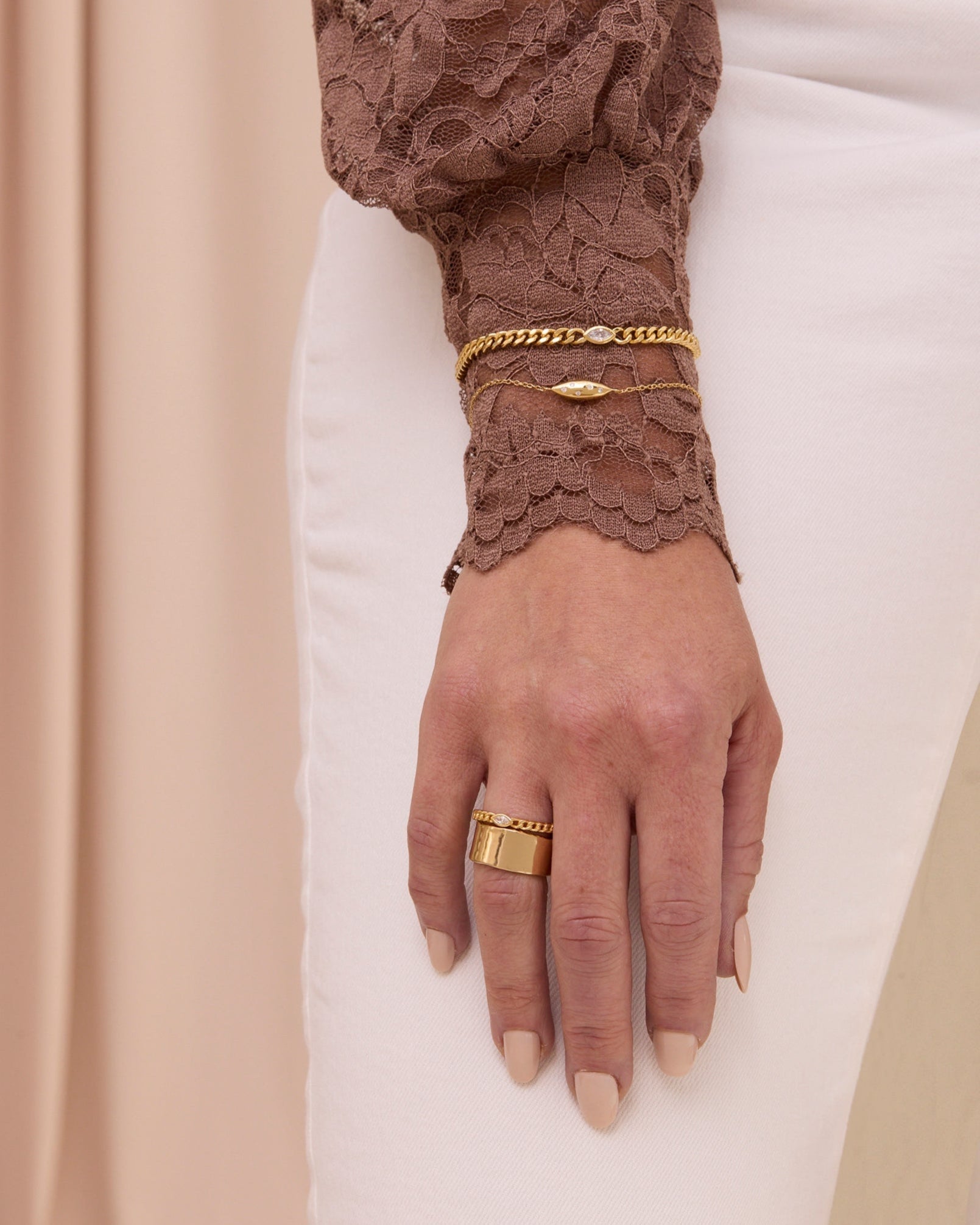Gold curb chain bracelet with white gemstone and a thin gold chain bracelet with puffy petal shape.
