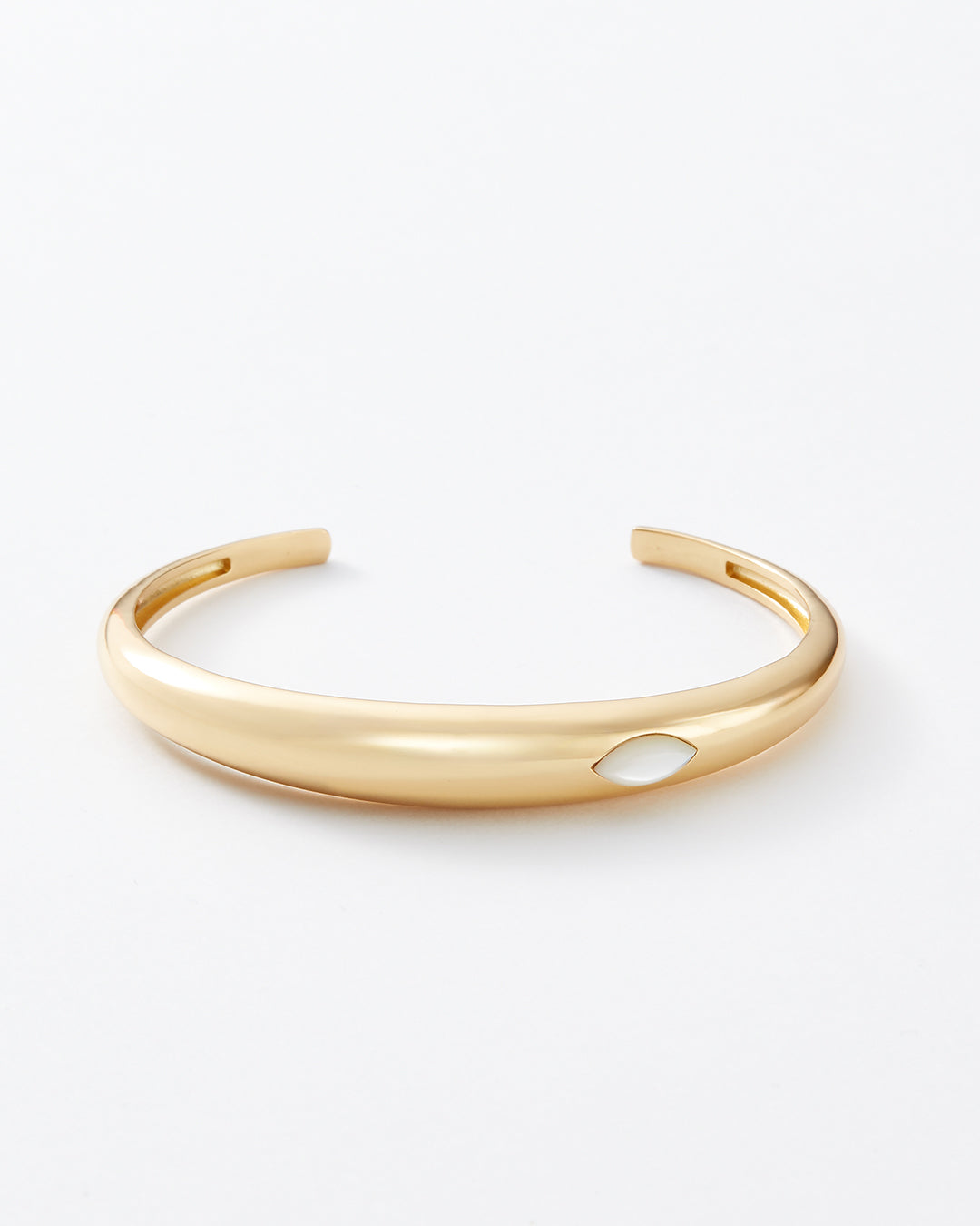 A polished gold-tone cuff bracelet with a small, smooth white inlay accent on the front, displayed on a clean white background.