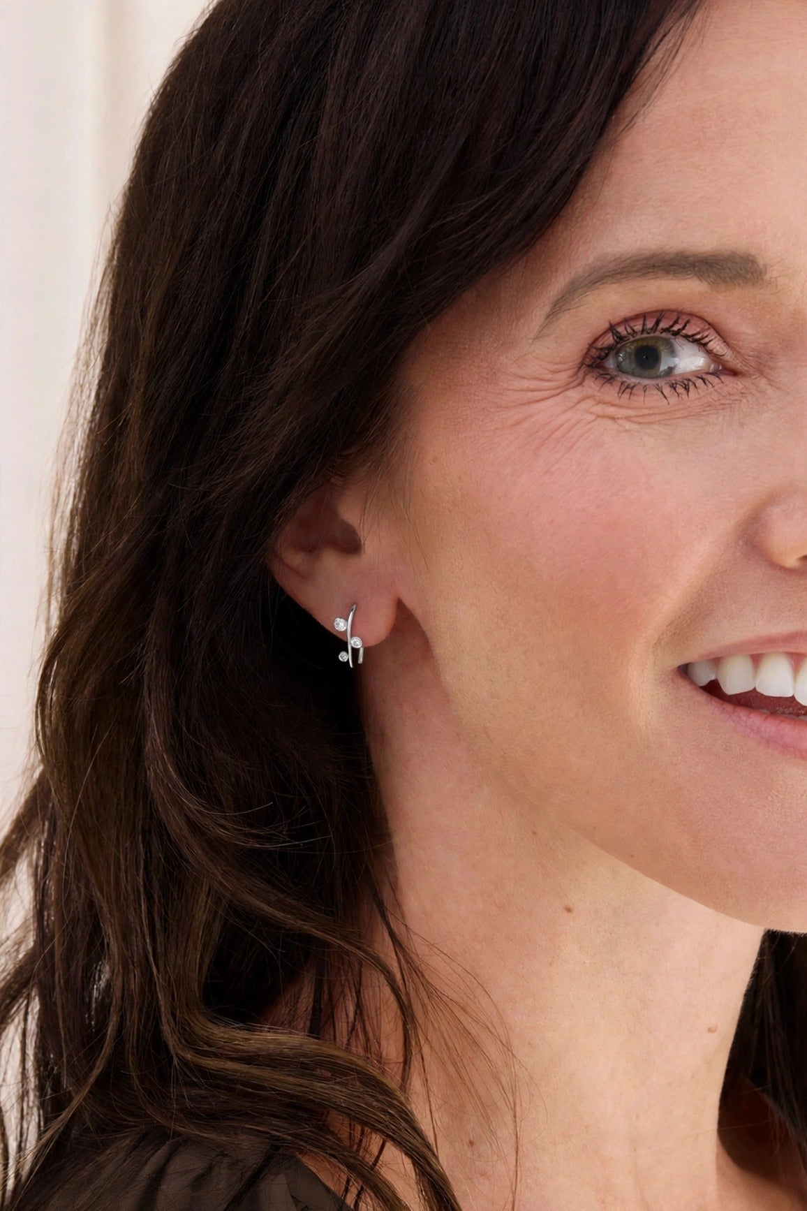 Aralia Tiny Hug sterling silver earring with three round white topaz stones, worn on a smiling model.