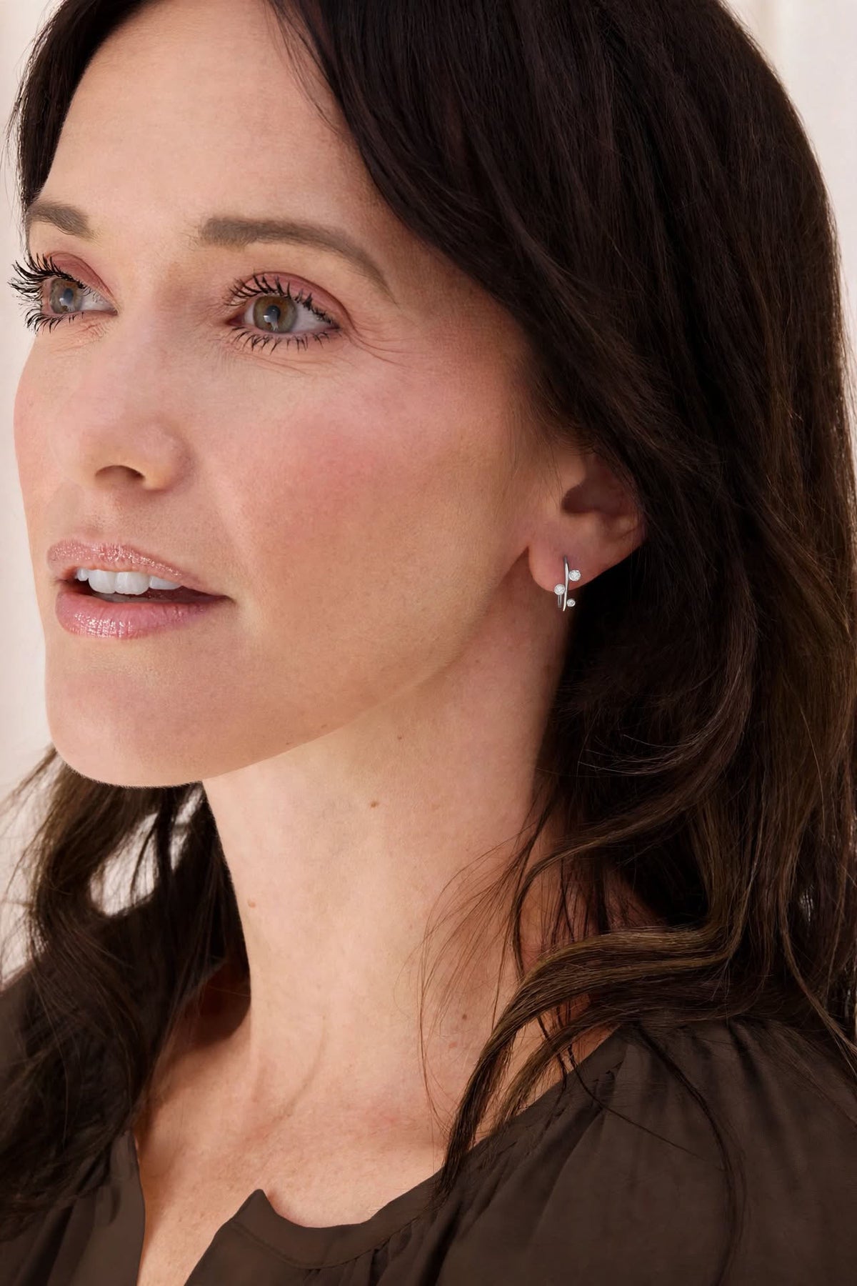 Close-up of an Aralia Tiny Hug sterling silver earring with three round white topaz stones, worn on a model’s ear.