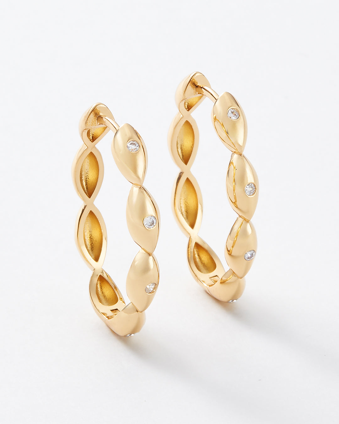 A pair of gold hoop earrings with a twisted, textured design and small clear gemstones, shown on a clean white background.