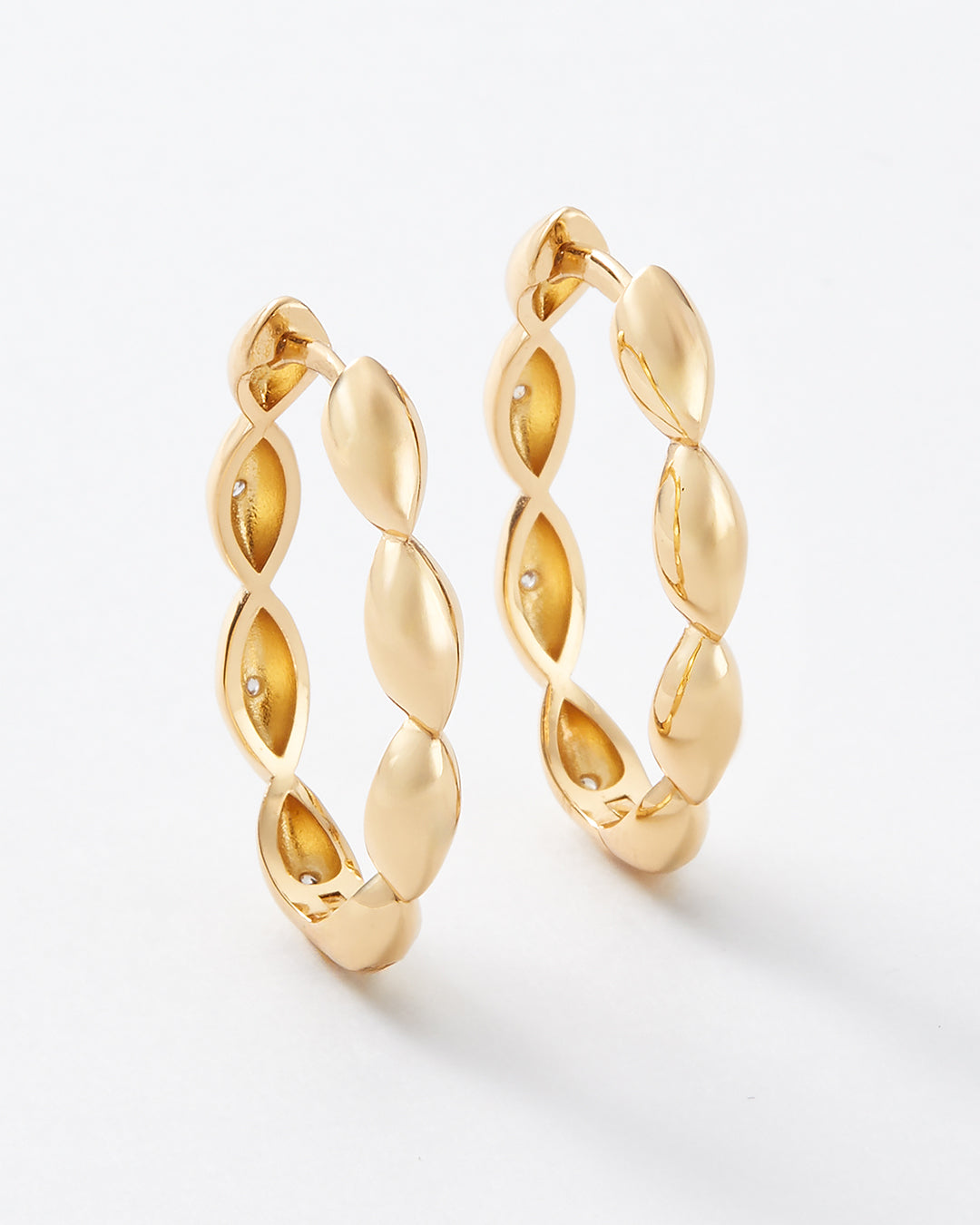 A pair of gold hoop earrings with a textured, twisted leaf-like design, shown on a clean white background.