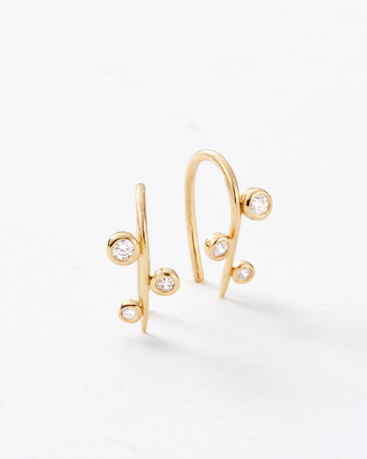 A pair of gold huggie threader hoop earrings with delicate curved branches and small bezel-set clear gemstones, photographed on a clean white background.