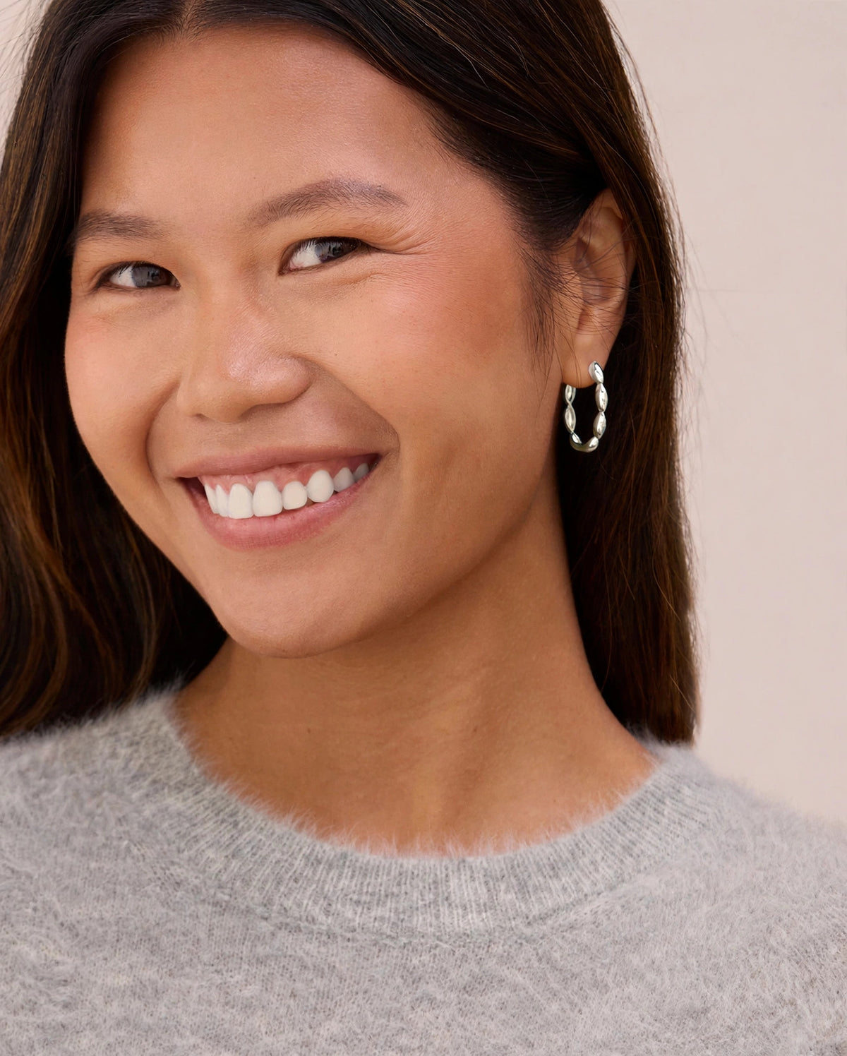 Wisteria reversible sterling silver hoop earring worn on a smiling model, showing the polished silver petal side.