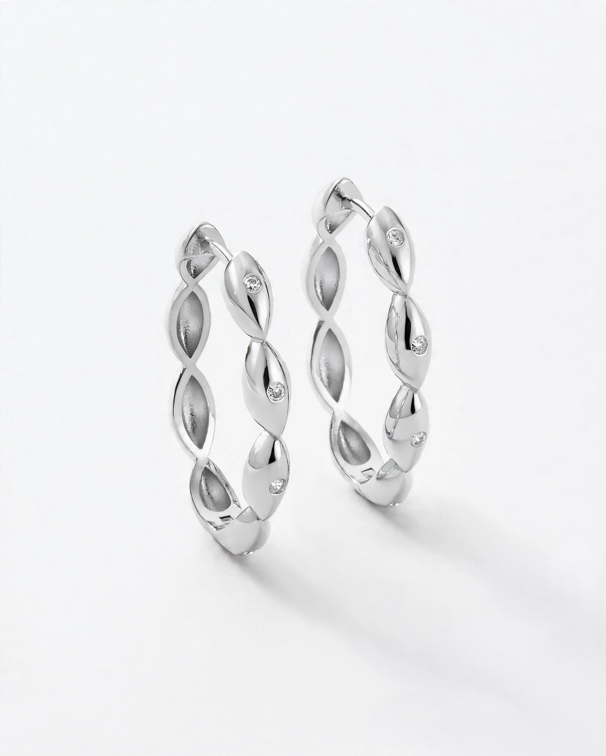 Silver large hoop earrings with a repeating petal shape. Earring is reversible. Front has white topaz gemstones that look like diamonds.