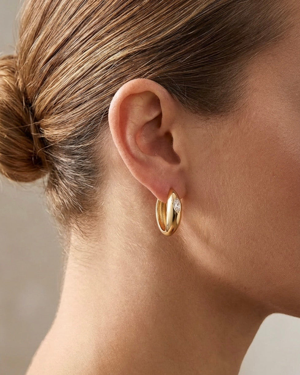A close-up side profile of a woman wearing a small gold hoop earring.