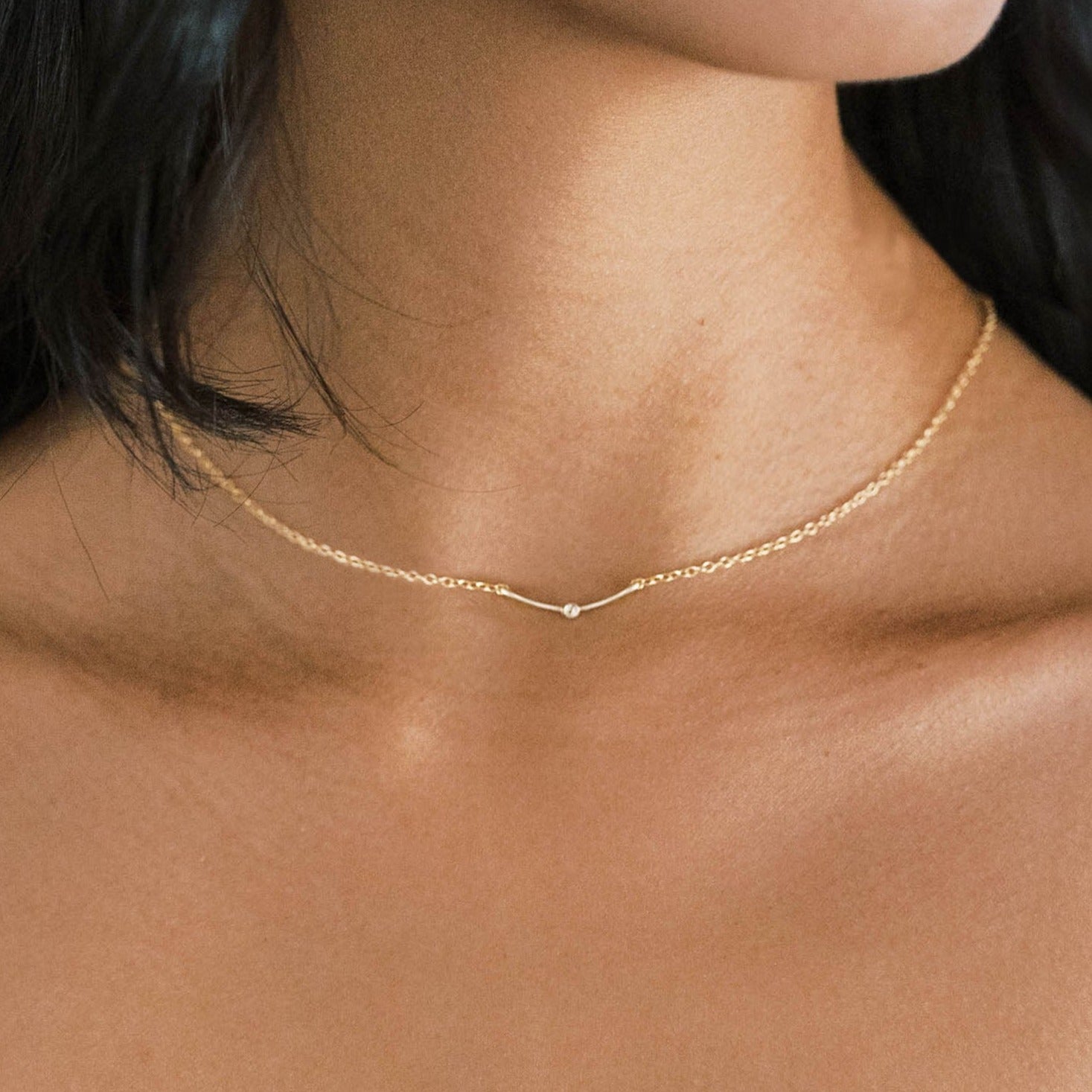 Thin gold chain with curved bar pendant. Small crystal gemstone in the center.