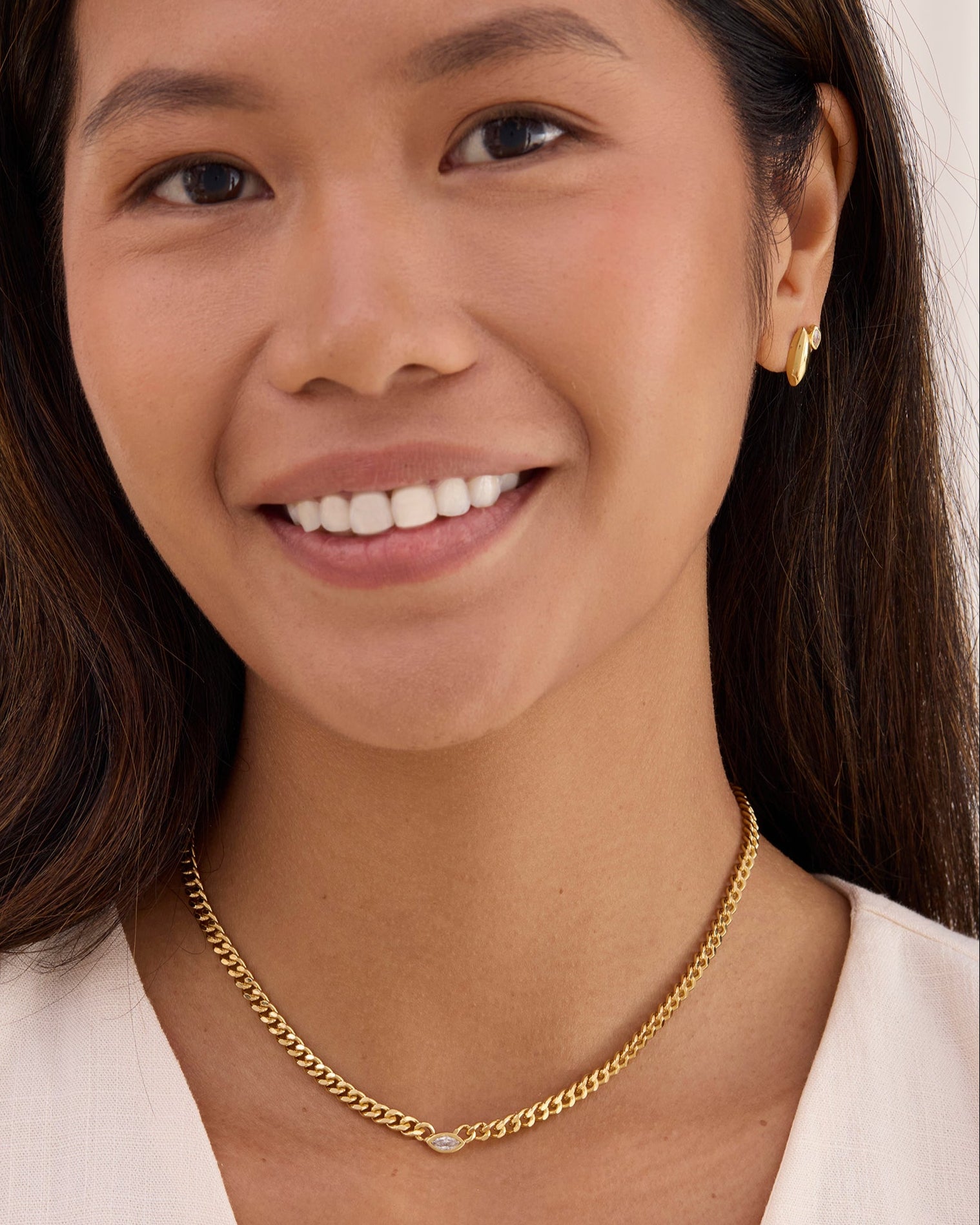 Women wearing a gold and gemstone earring and a curb chain necklace.