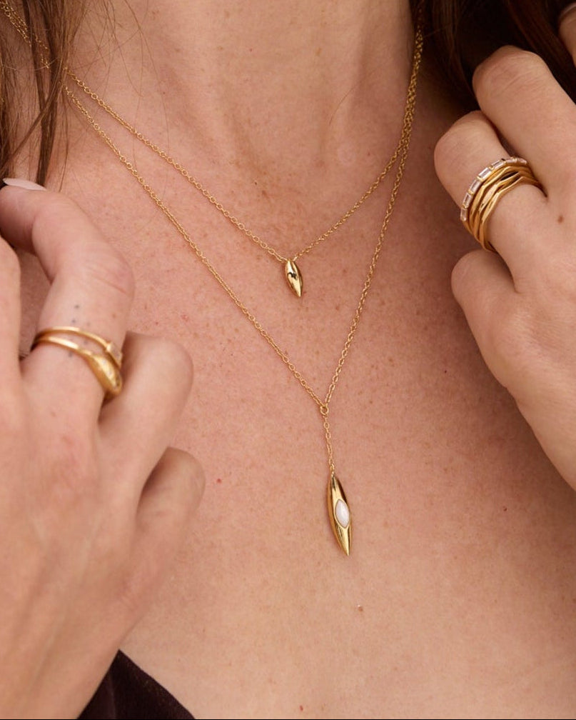 Woman wearing layered gold necklaces made with white topaz. and a ring on her finger.