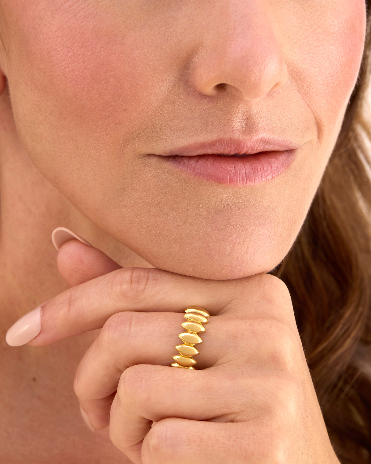 A close-up of a woman's hand and lower face wearing a gold ring with a textured, segmented snake-like design.
