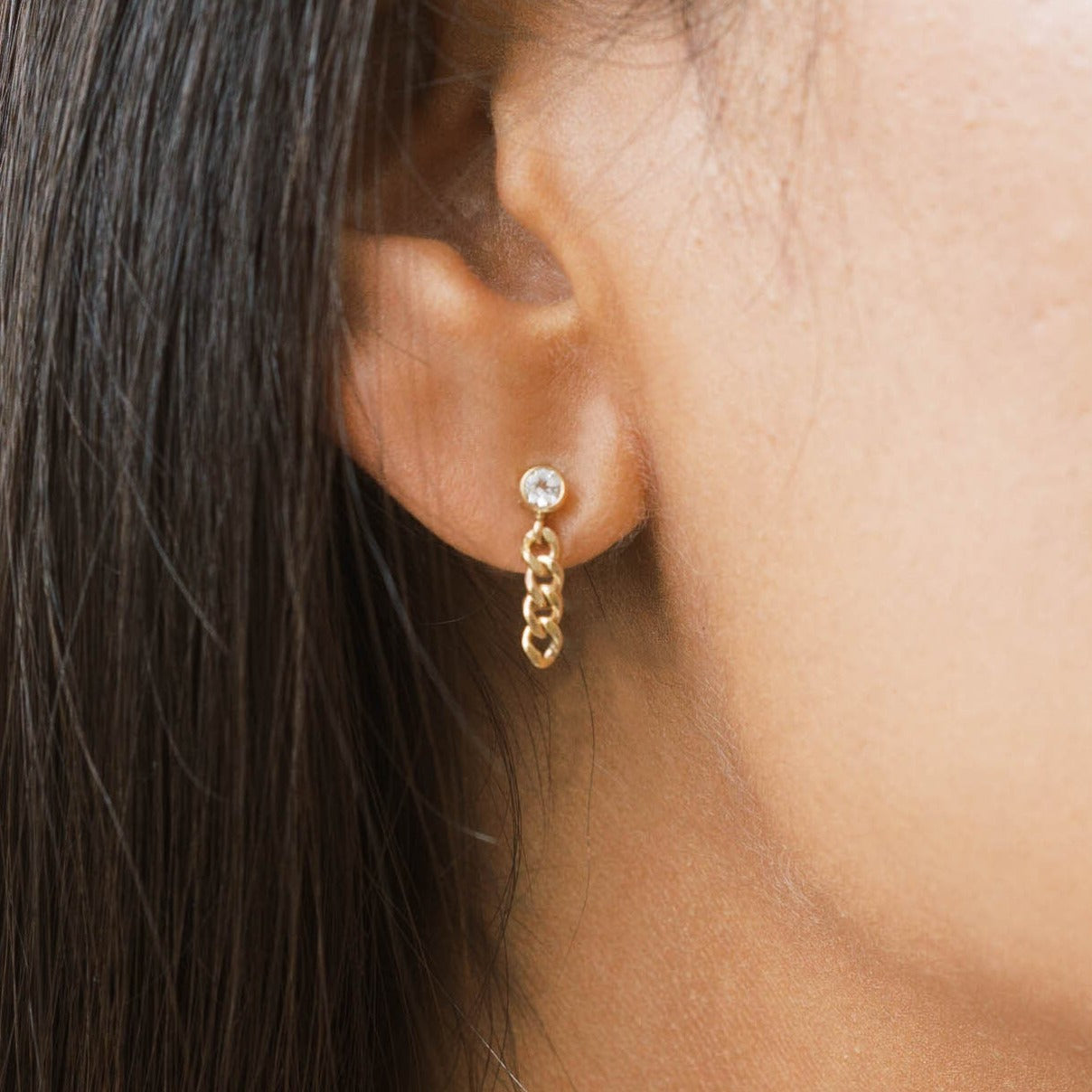 White topaz stud earring with a gold chain hanging down.