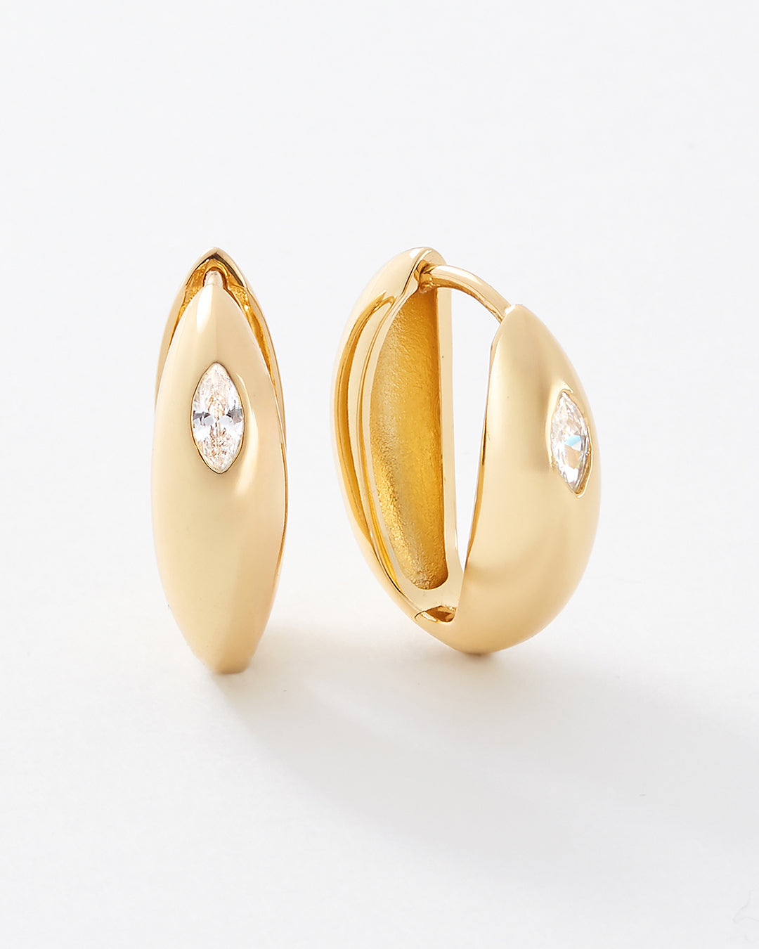 A pair of gold huggie hoop earrings with a small marquise-cut white topaz gemstone on the front, shown on a clean white background.