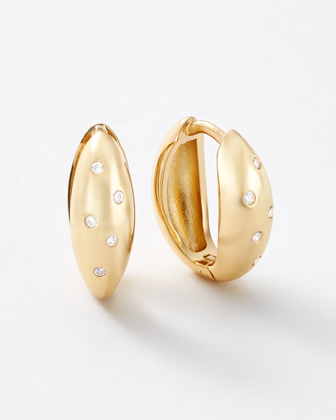 A pair of gold huggie hoop earrings with small clear pavé-set stones, shown on a clean white background.