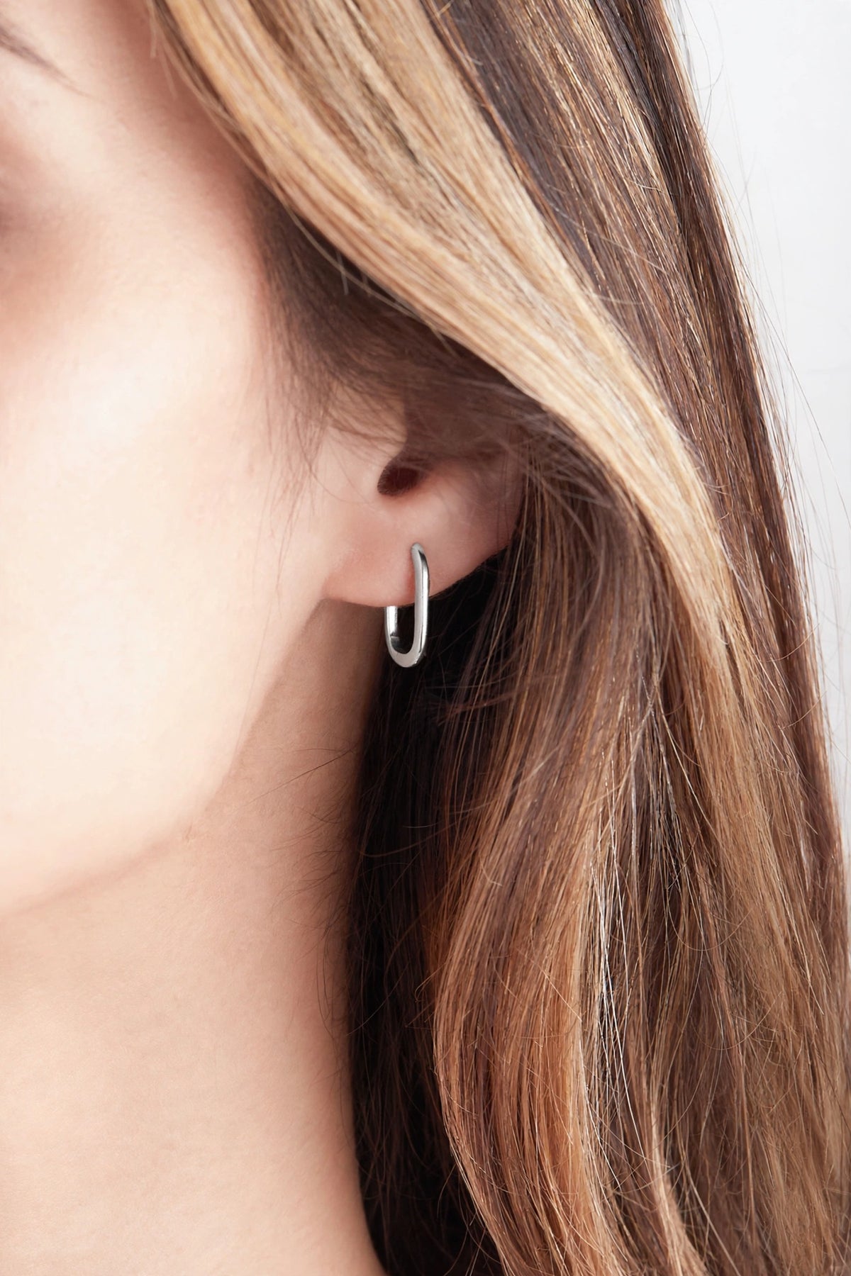 Midi reversible sterling silver hoop earring worn on a model, showing the smooth polished silver side.