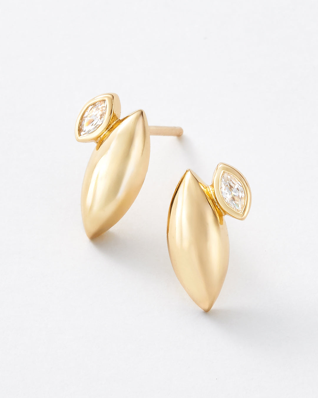 A pair of gold leaf-shaped stud earrings with marquise-cut clear gemstones, shown on a clean white background.