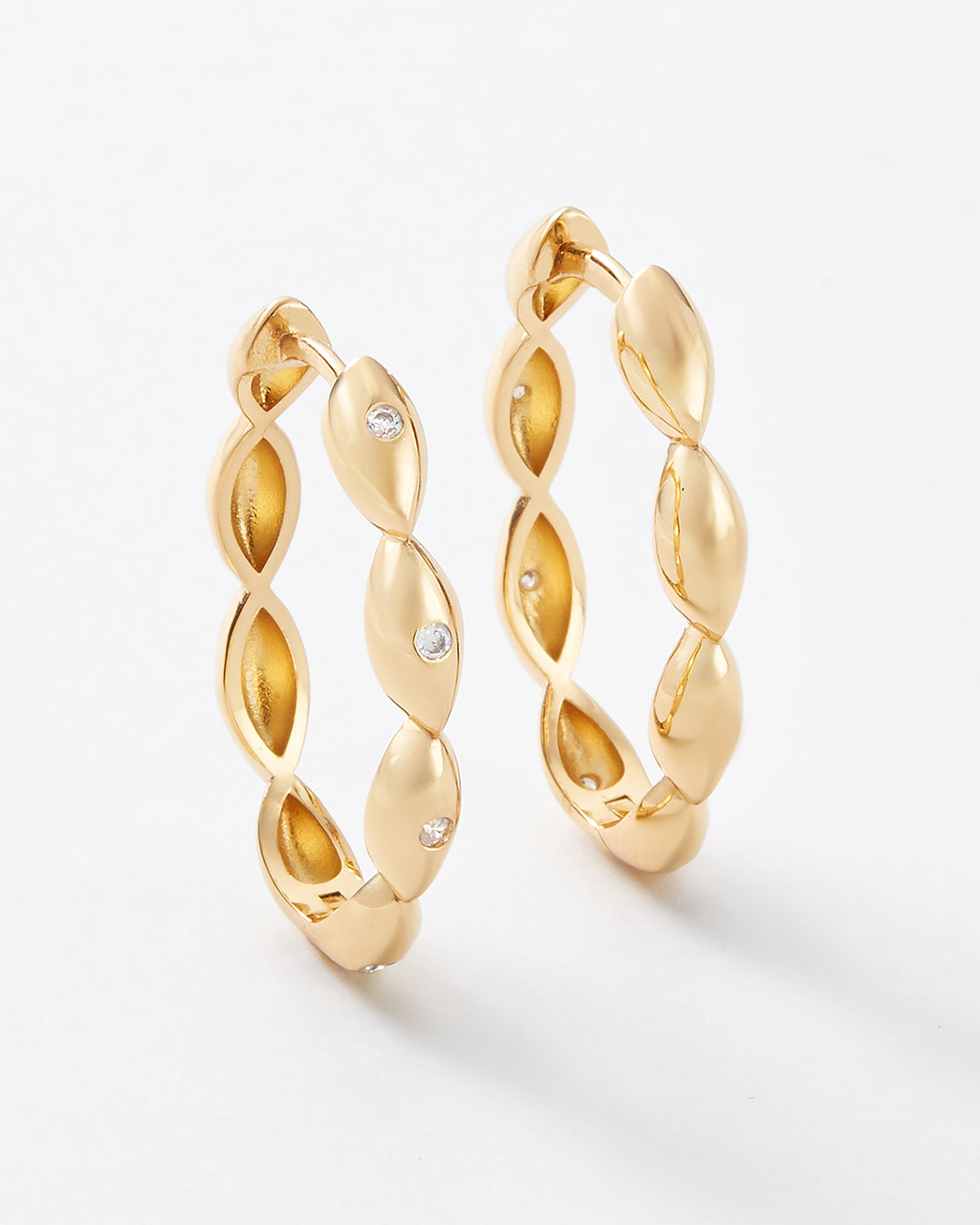 A pair of gold hoop earrings with a twisted, leaf-like textured design and small clear crystal accents, shown on a clean white background.