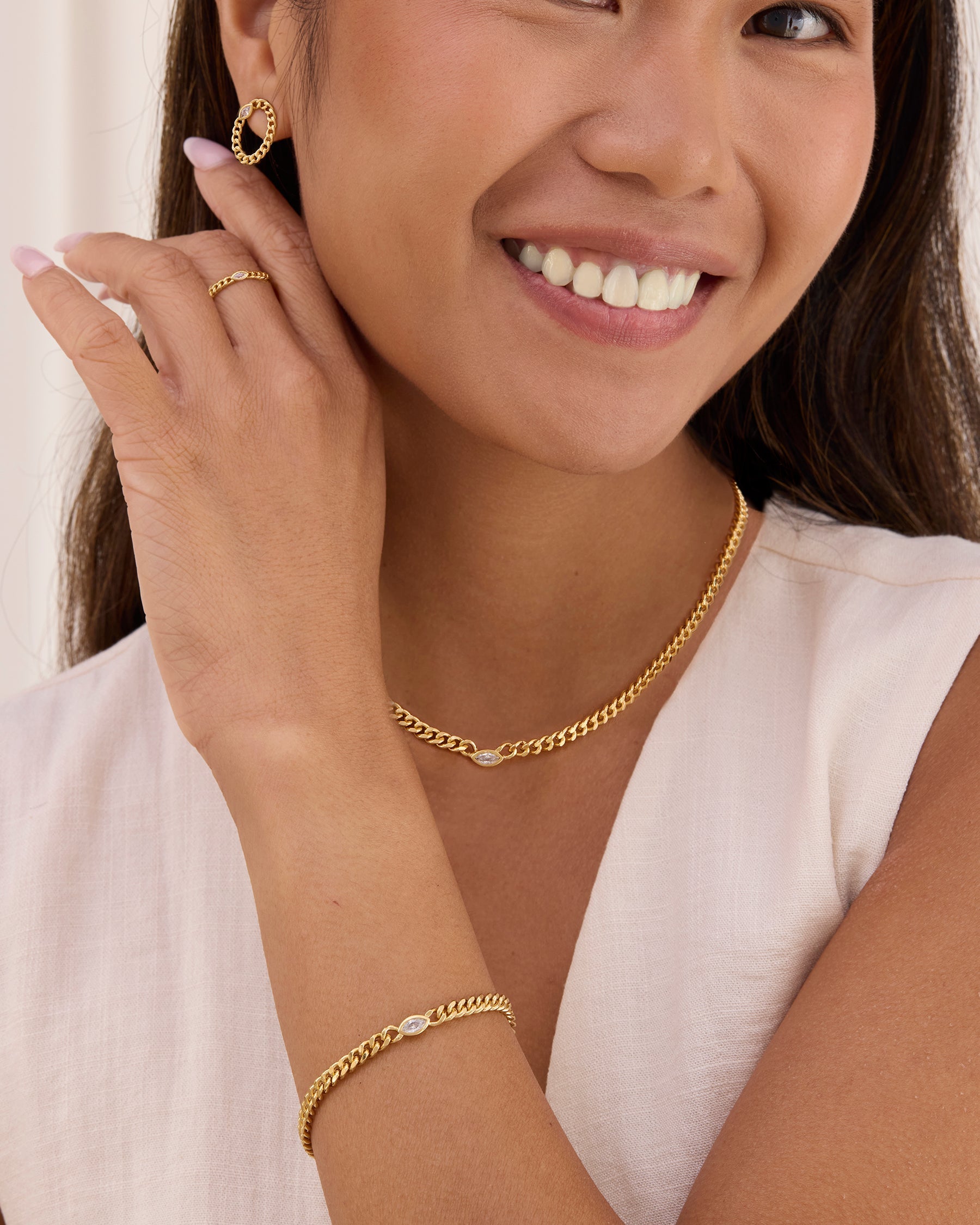 Woman wearing gold curb chain jewelry including earrings, necklace, and bracelet.