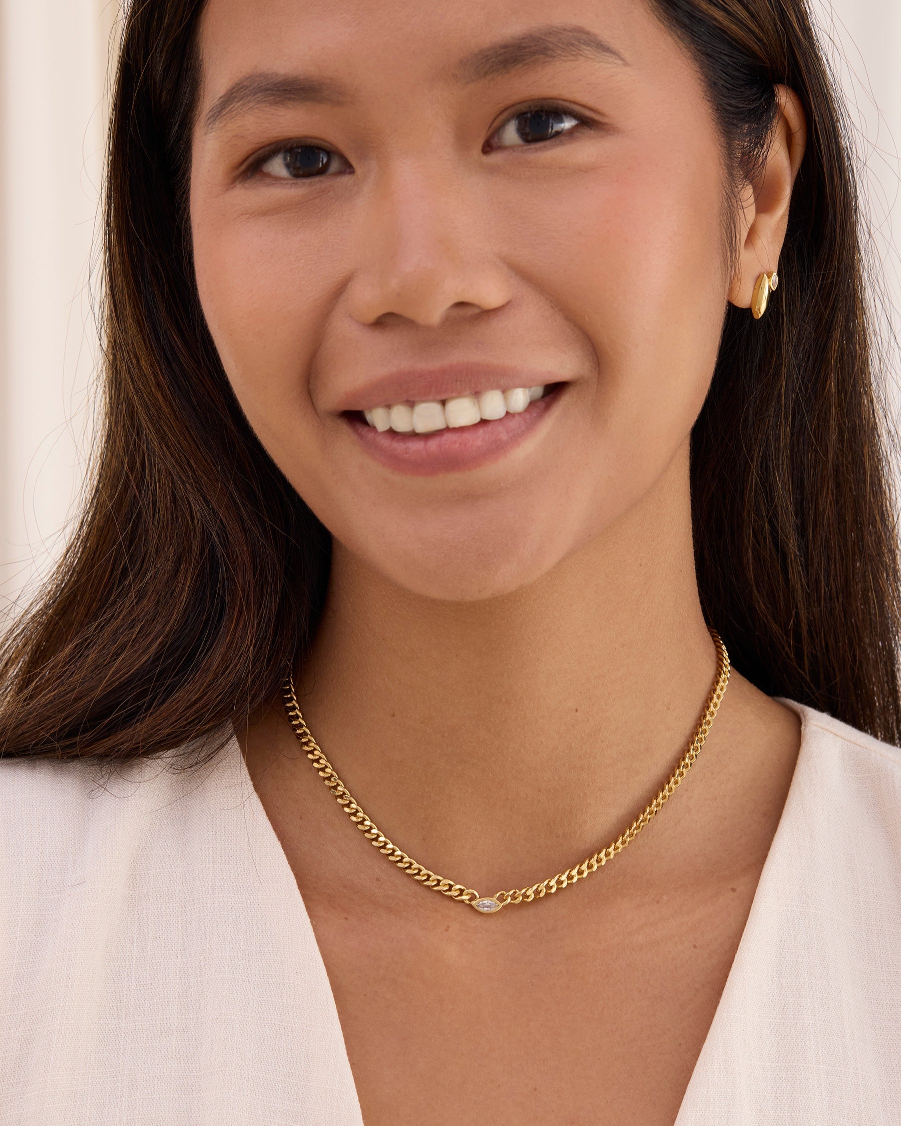 Woman wearing a gold curb chain necklace with a white topaz marquise