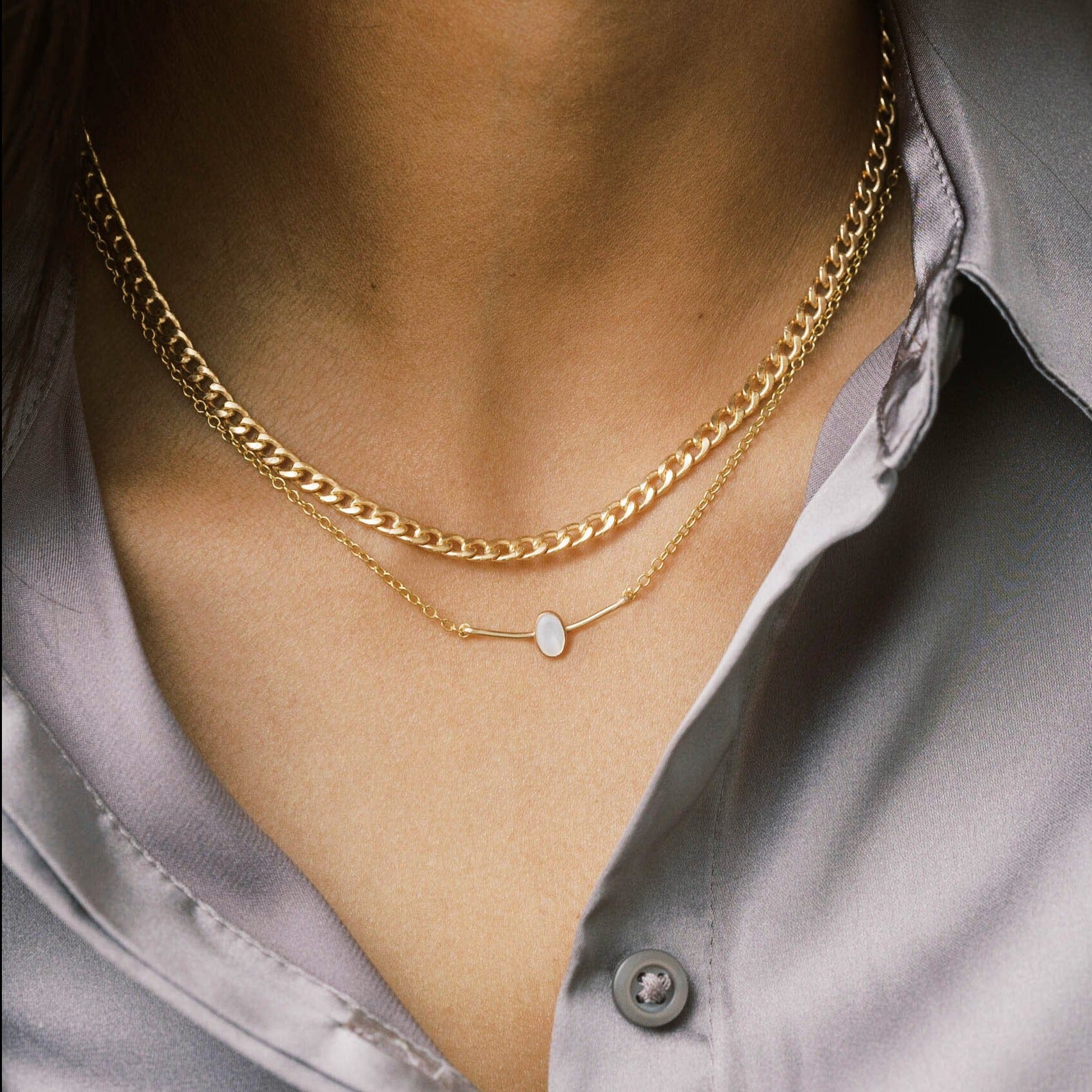 Two gold layering necklaces. One with a pearl set on a curved bar pendant. The other is a bold curb chain.