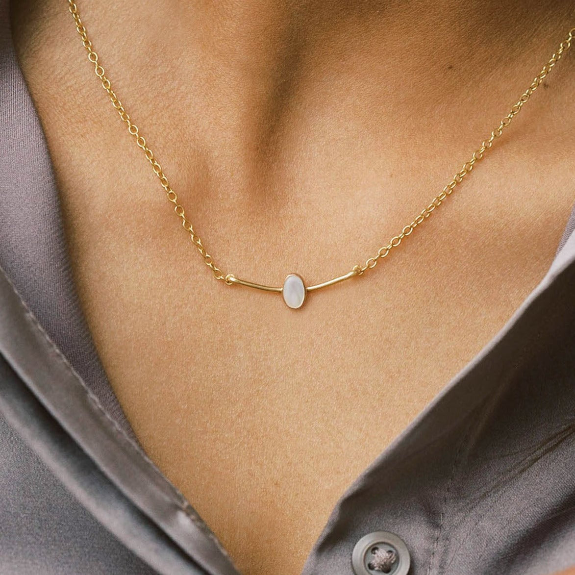 Small gold curved bar pendant with a pearl in the center.
