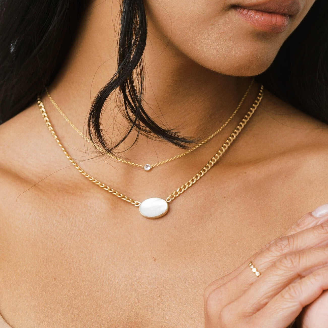 Thick gold chain necklace with a pearl pendant layered with a thin necklace with white topaz pendant.