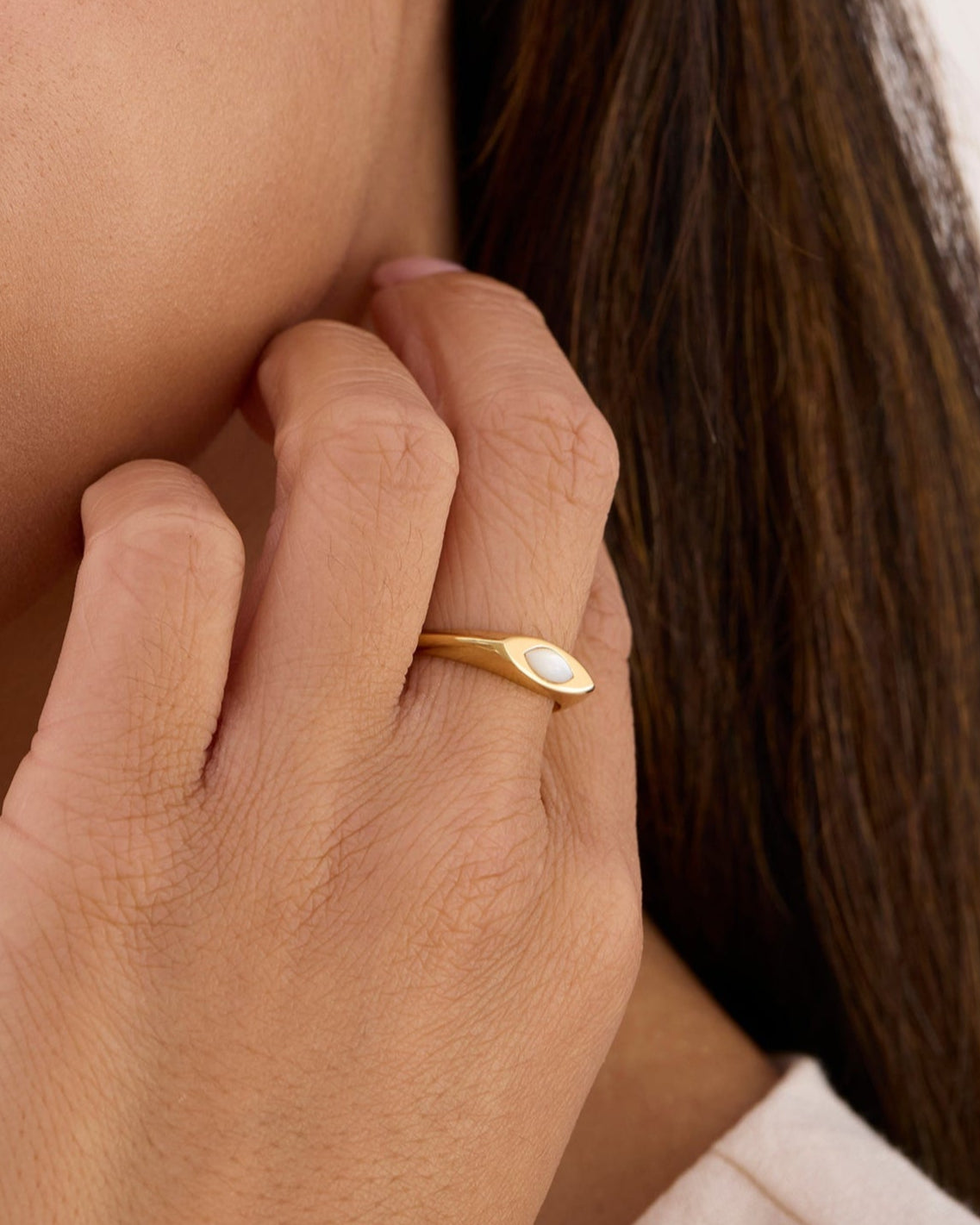 Women wearing gold huggie marquise pearl earrings and a signet ring.