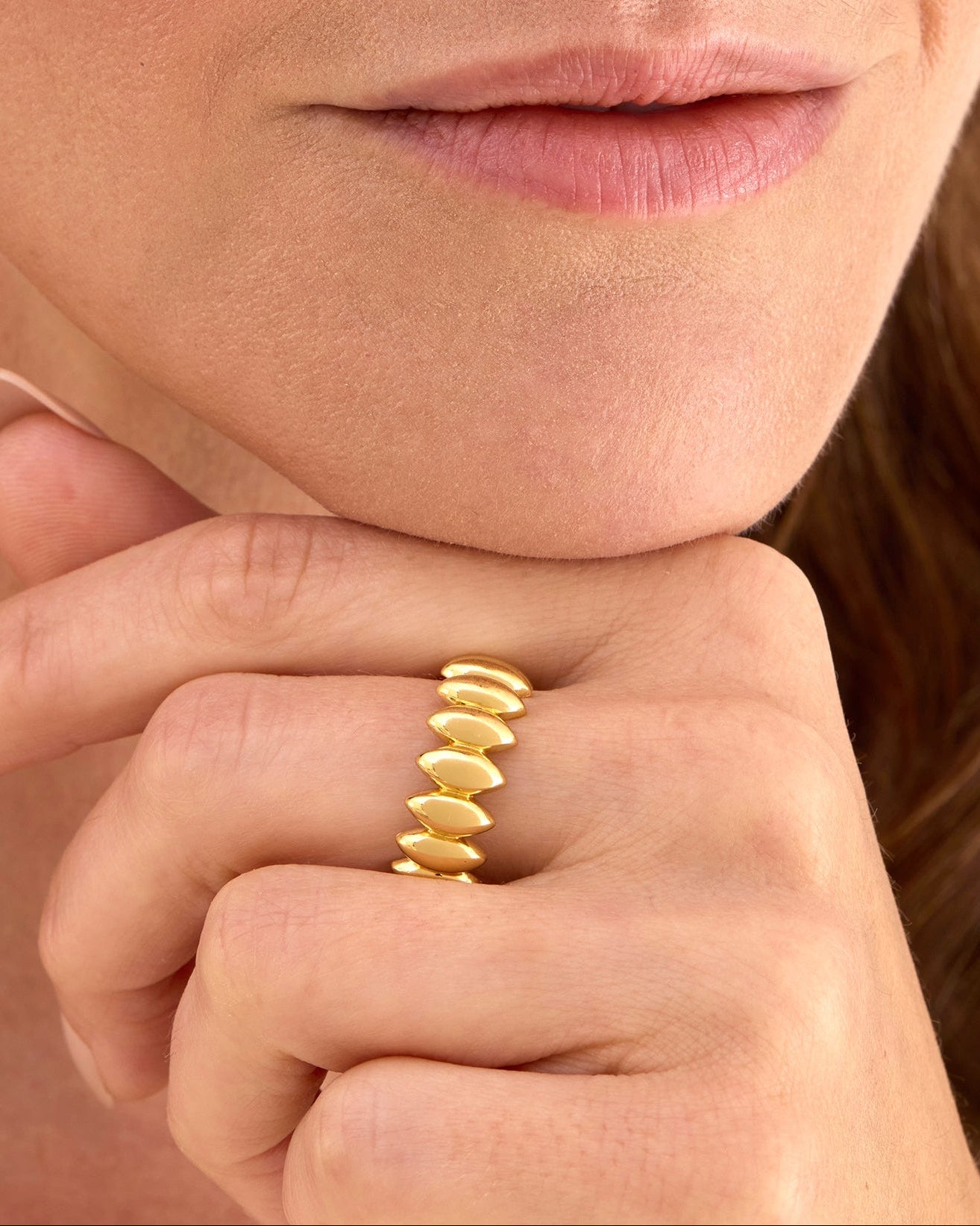 Close-up of a gold wide ring with a repetitive petal shape wrapping around finger.