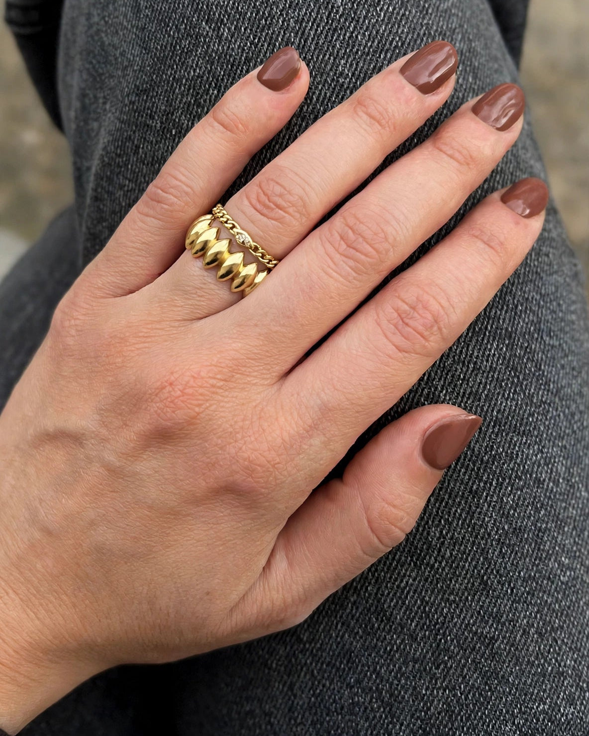 A close-up of a hand wearing a textured gold ring, resting on dark gray denim fabric.