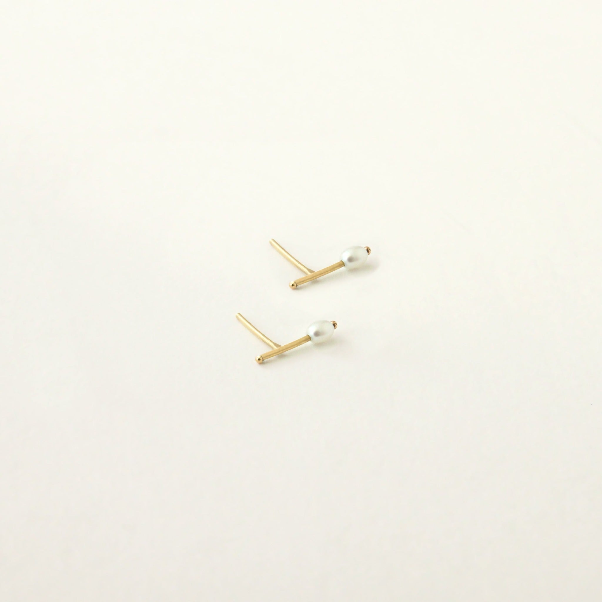 Dainty thin gold bar stud earring features a small oval pearl and small gold ball details on ends of the bar.