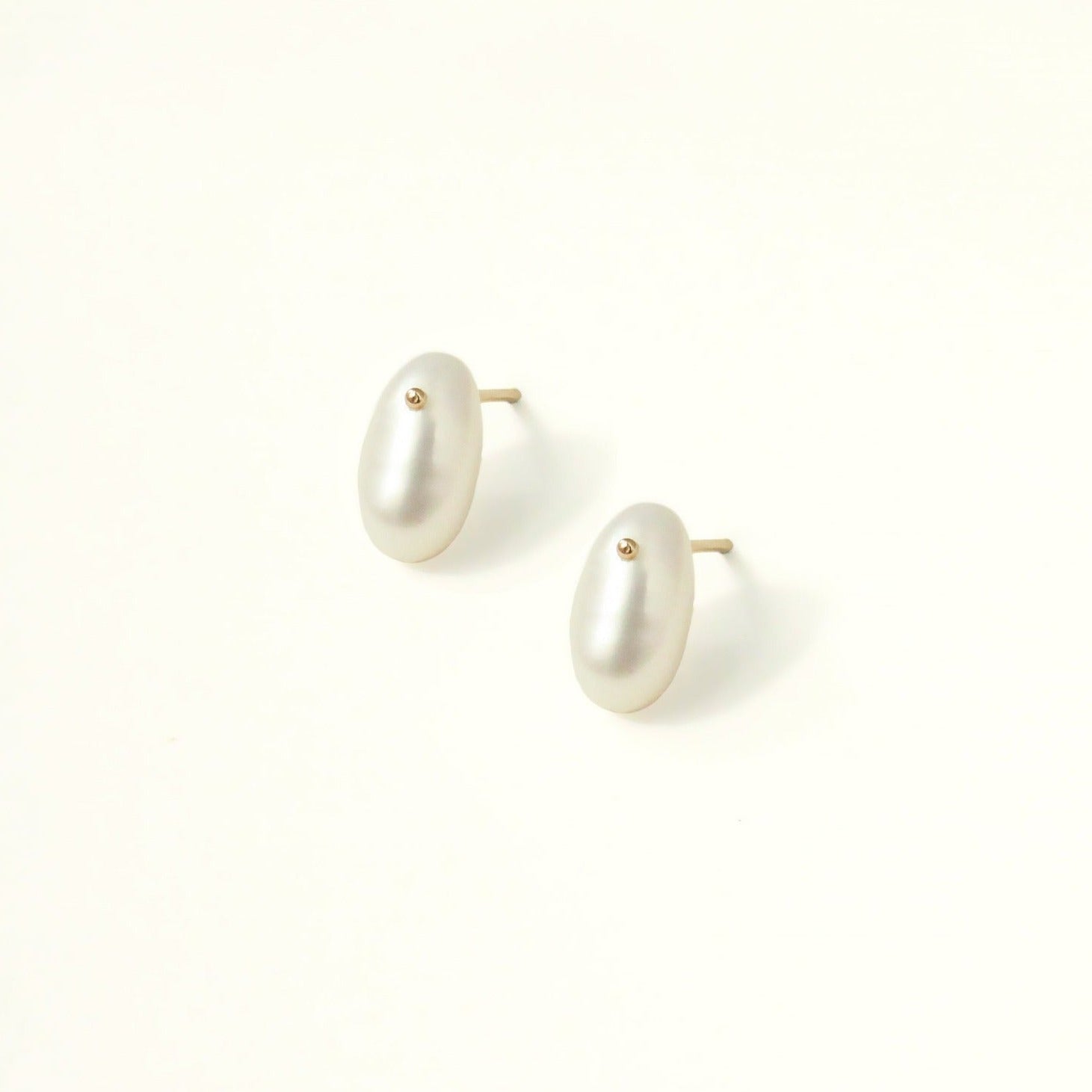 A minimalist pearl earring. The oval pearl has a small gold dot at the top, which is a sparkly unique feature. The studs are sophisticated with their simple and feminine shape.