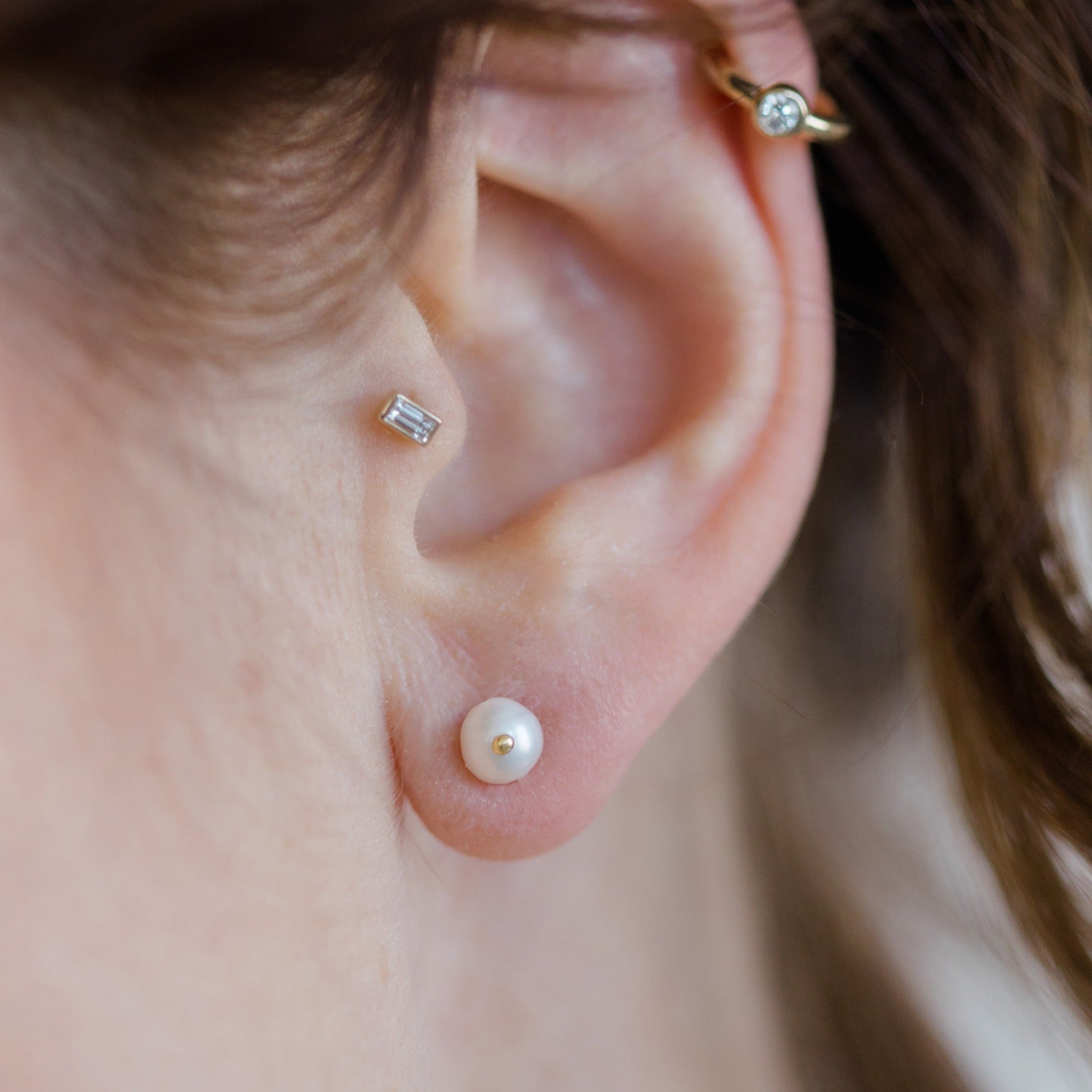 The round pearl stud earring is shown here with other diamond stud earrings. You can create your own curated ear party with this pearl stud earring.