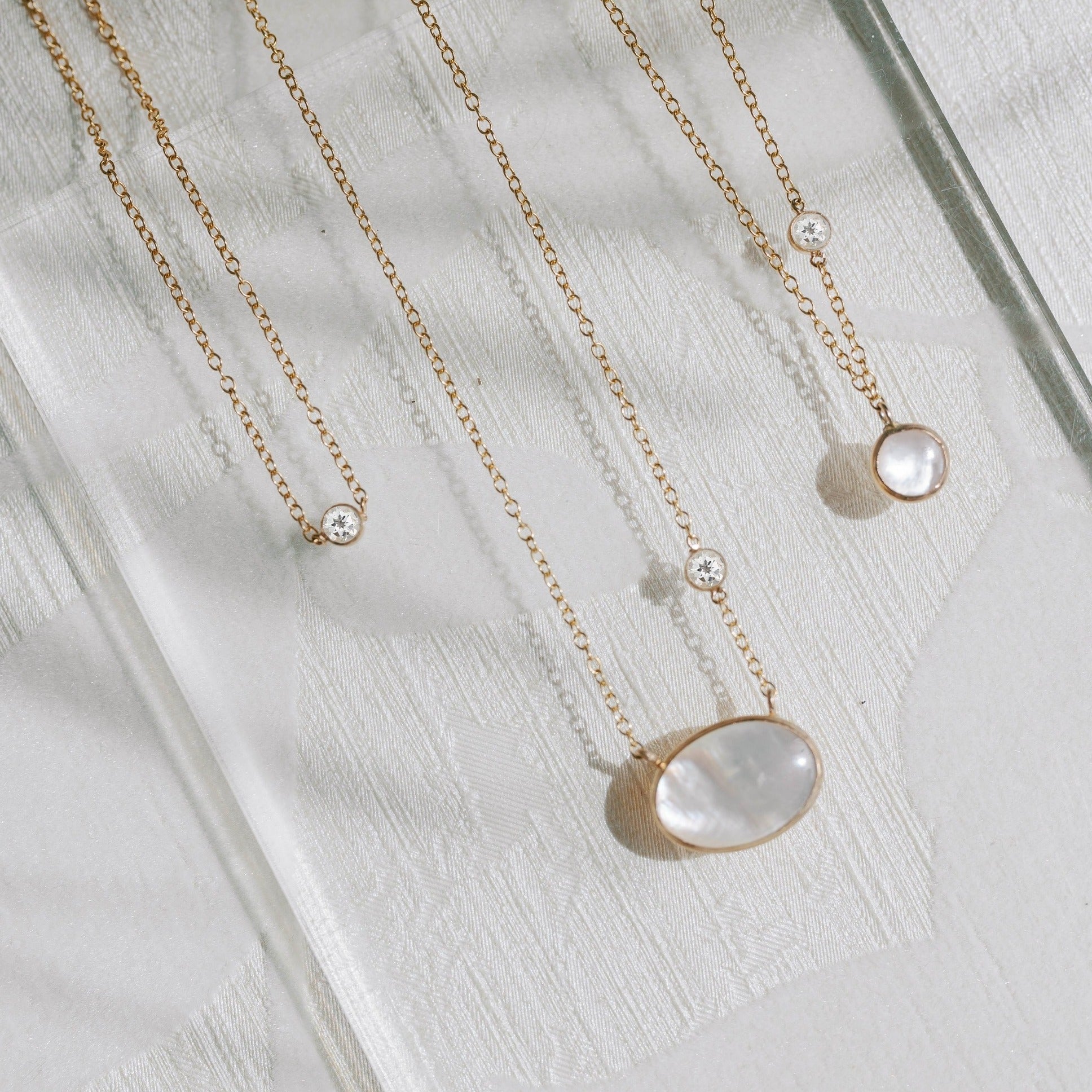 Mother of pearl pendant necklaces featuring small white topaz stones. The gold is recycled